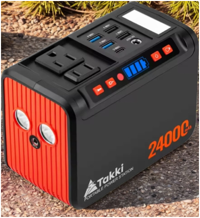 Black and red 2400C portable power station with AC and USB ports, shown on a rocky outdoor ground near pine needles, ready for off-grid use.