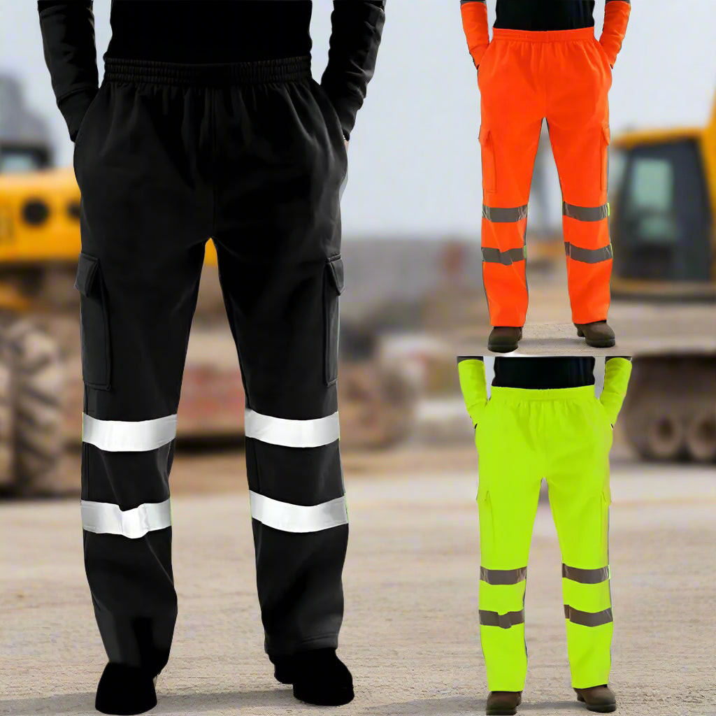 Three pairs of high-visibility reflective safety work pants in black, neon yellow, and safety orange displayed in front of a blurred construction site background with heavy machinery.