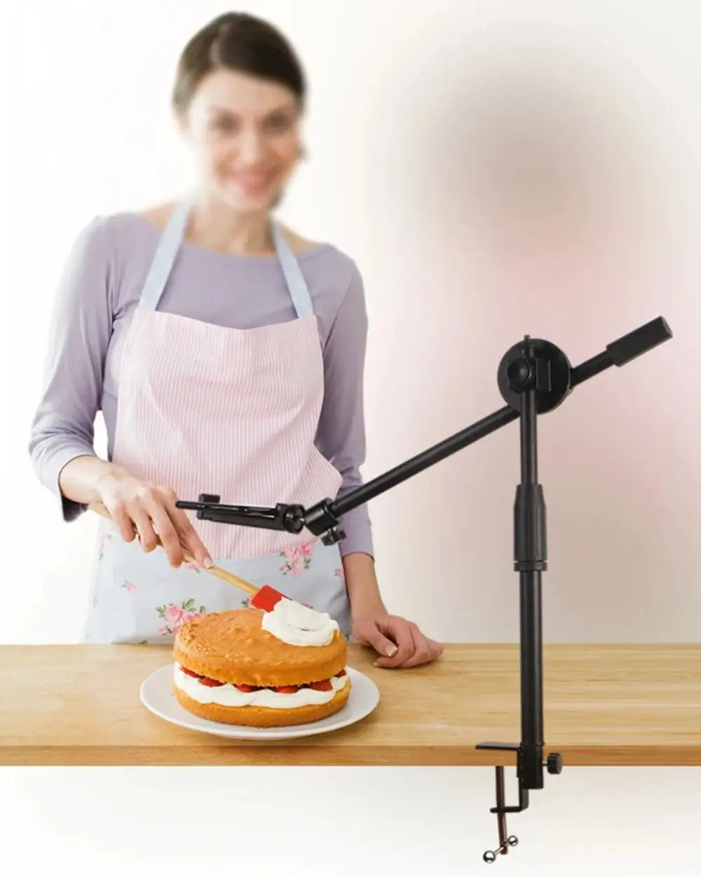 The overhead tripod phone mount is being used by a woman to film from above, while she frosts a cake.